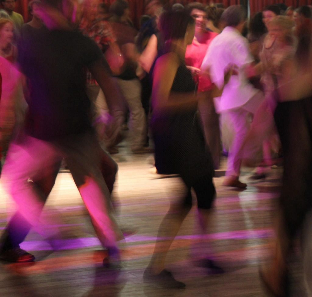Dancing people, with lively footwork, and a wooden dancefloor with evening lighting.